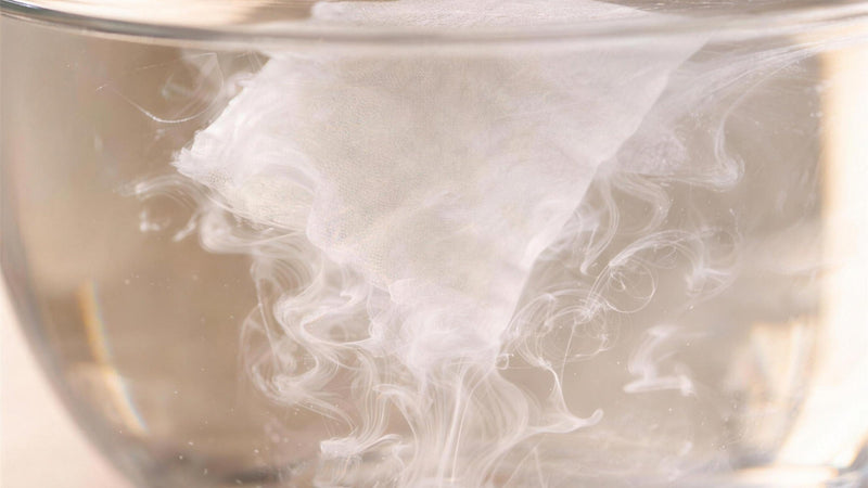 A DSSLV cleaning sheet dissolving into soft white swirls in a glass bowl of water