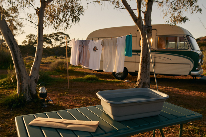 Laundry drying on a line between gum trees beside a retro caravan at an Australian bush campsite