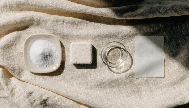 Dishwasher detergent formats side by side on cream linen: powder, tablet, gel and a dissolvable sheet